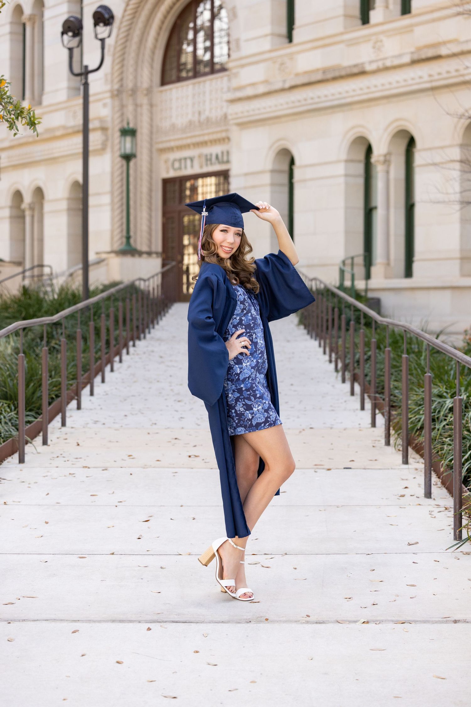 Two graduates in blue gowns toss caps in the air outside a classic university building.