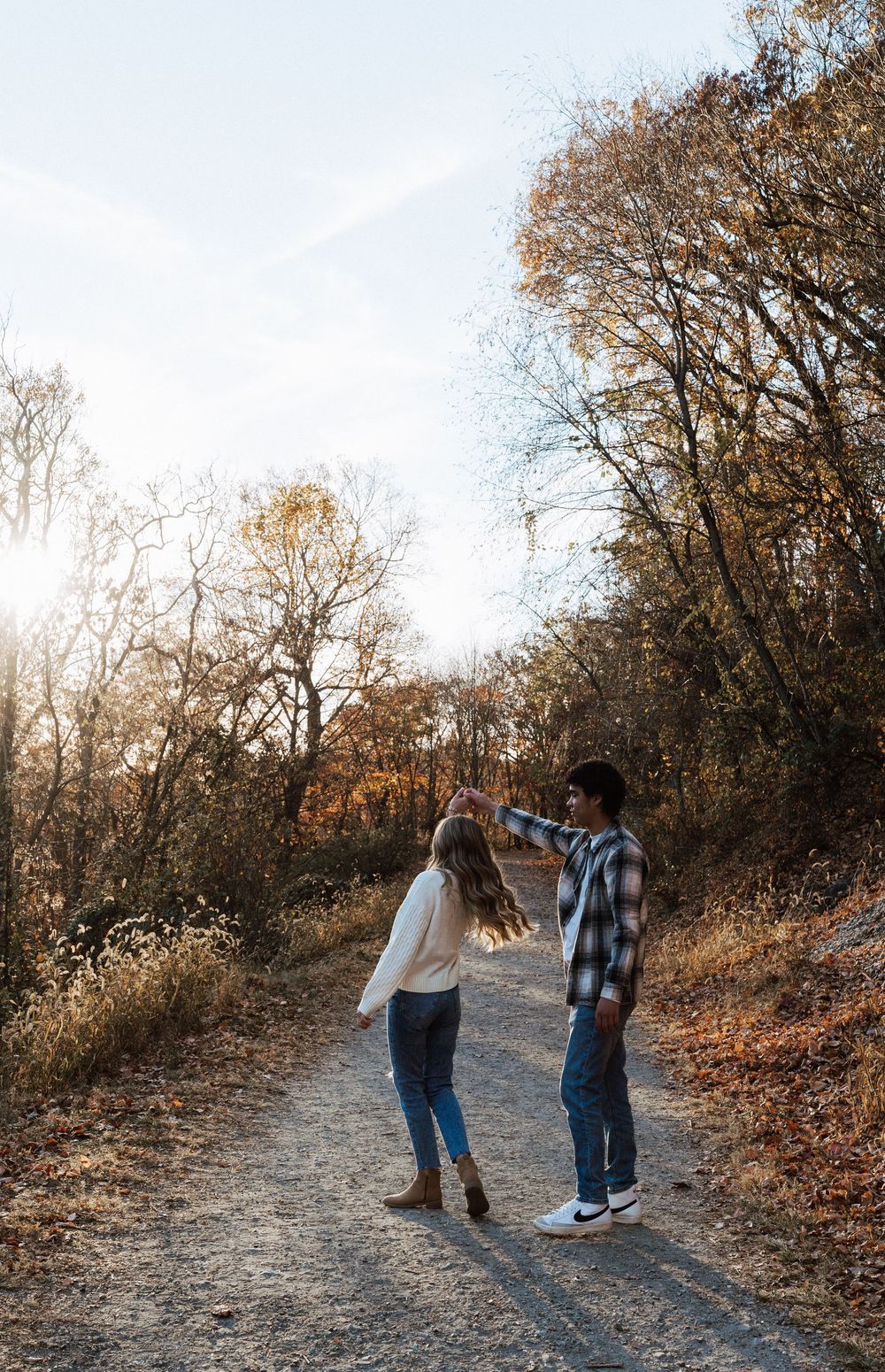 A couple dances on a scenic autumn trail surrounded by golden trees in warm fall sunlight.