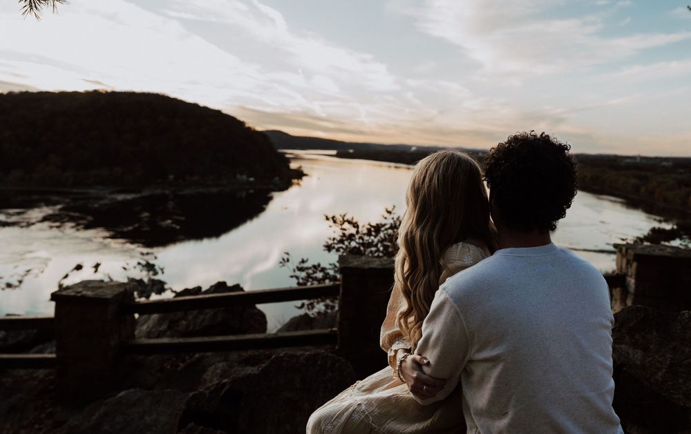 Couple sitting together on a rocky overlook enjoying a scenic river valley view at sunset.