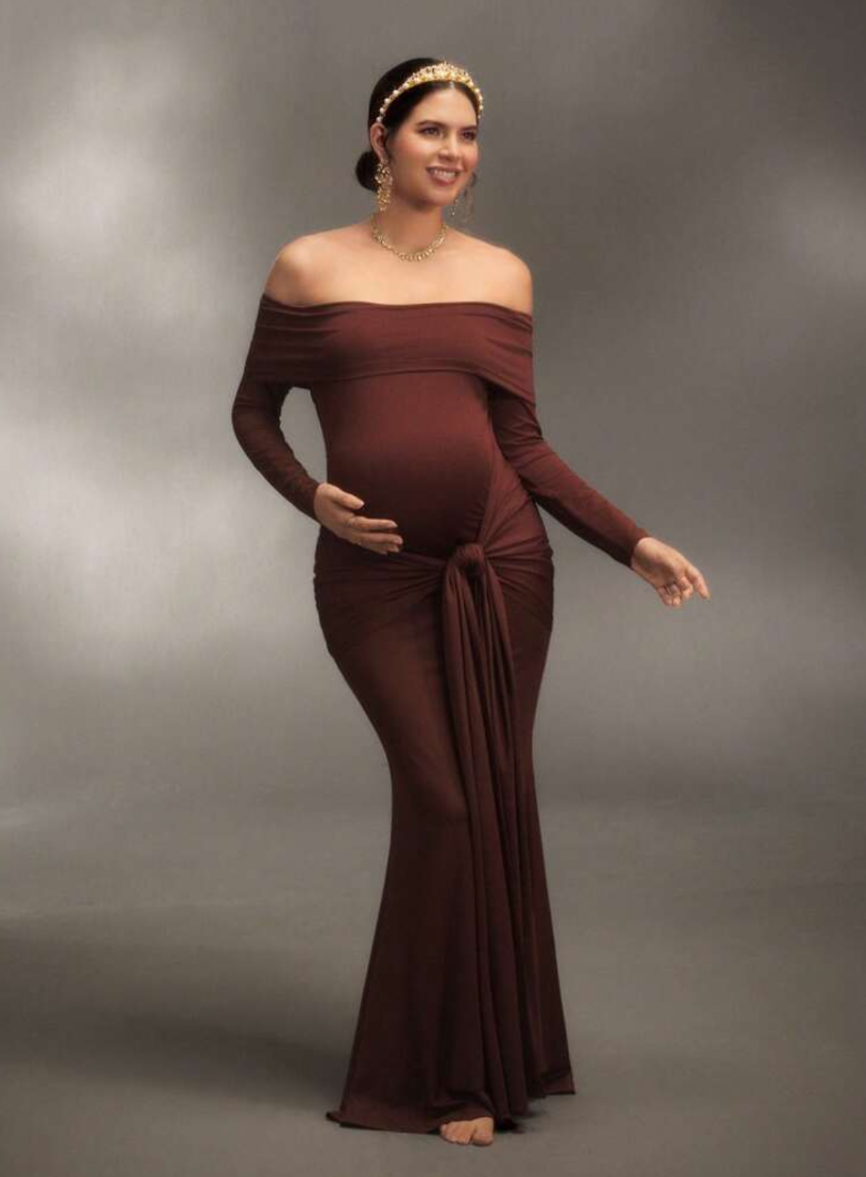 Pregnant woman in brown off-shoulder maternity gown with gold headpiece, posing gracefully for maternity photoshoot.