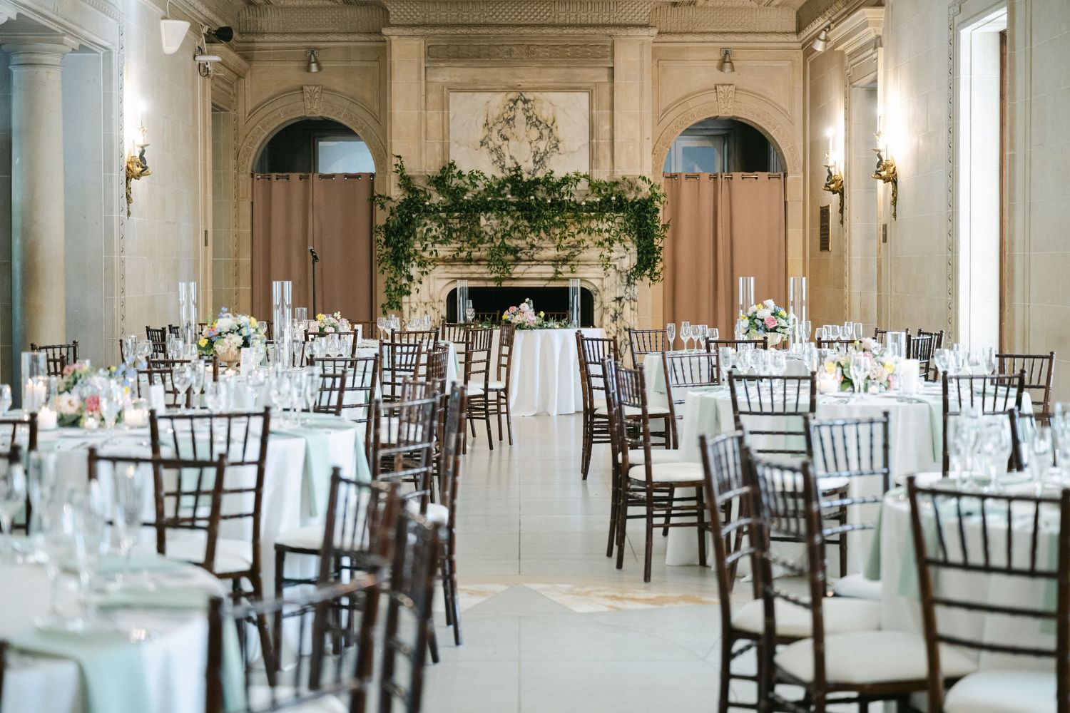 Armour House Wedding - Elegant wedding reception hall with chiavari chairs, white linen tables, floral fireplace backdrop.