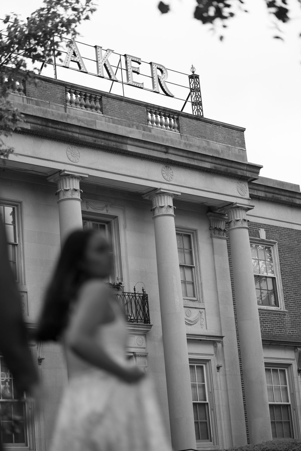 Woman in white dress stands before a grand columned Baker building in black and white photo.