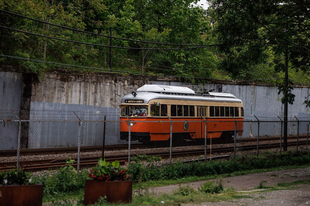 Vintage orange and white PCC streetcar traveling along outdoor railway tracks.