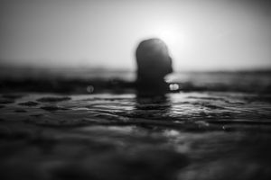 Silhouette of a person submerged in calm ocean water at sunset in black and white.