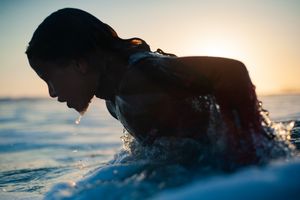 Surfer paddling through ocean waves at sunset with golden light reflecting.
