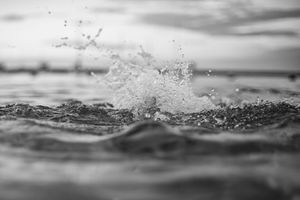 Black and white close-up of ocean wave splashing against water surface.
