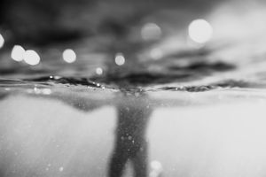 Black and white underwater photography showing water surface with bokeh light reflections and bubbles.