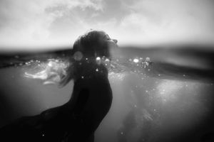 Black and white underwater photo of a person swimming at the ocean surface with light bubbles.