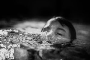 Black and white photo of a child swimming with head just above water surface.