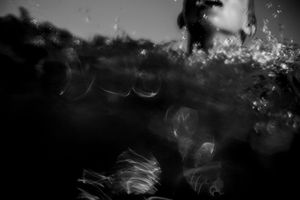 Abstract black and white underwater photo showing blurred figure and light bokeh through ocean waves.