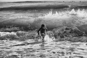 Black and white photo of a child running through crashing ocean waves on a sandy beach.