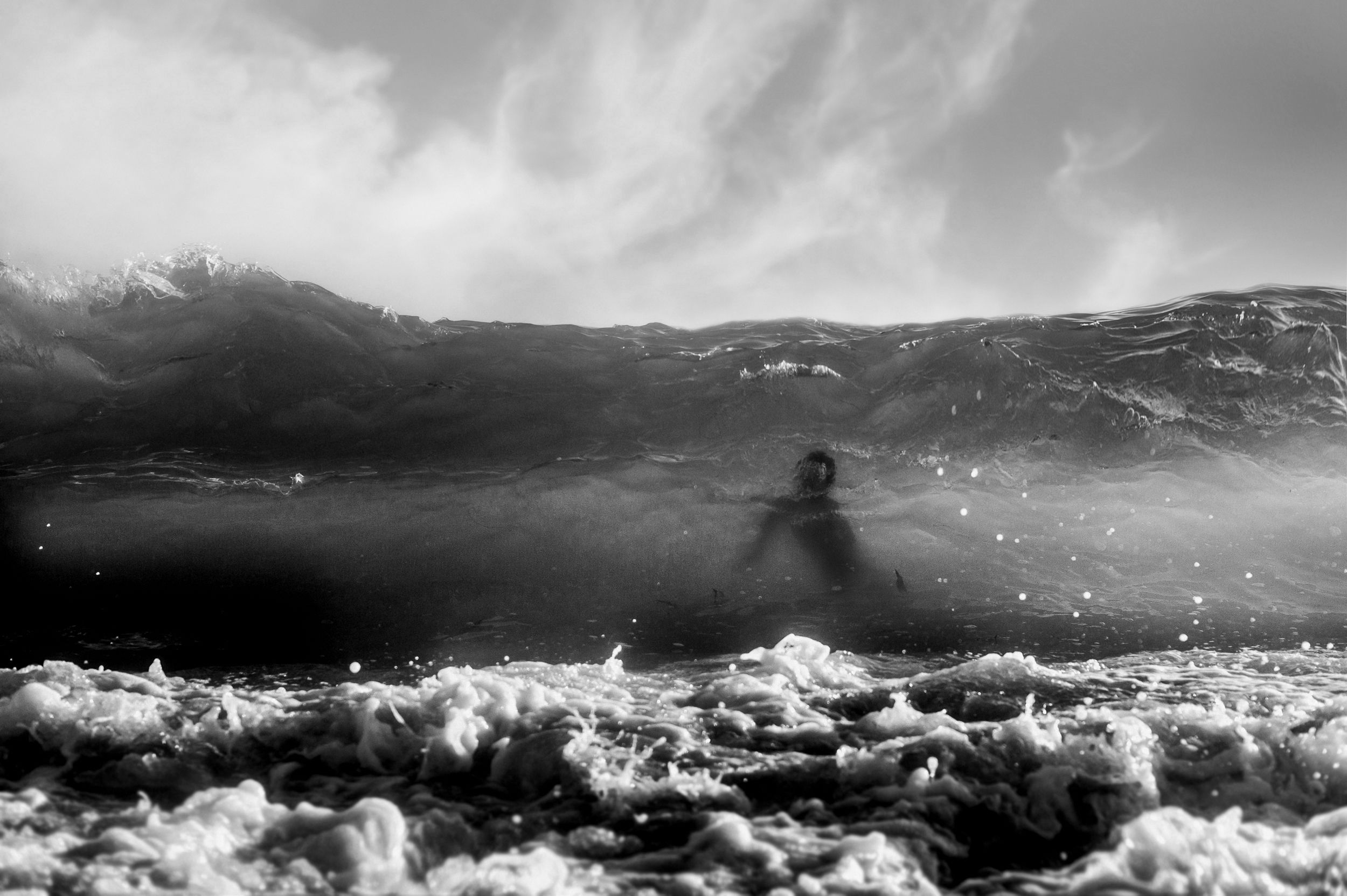 Black and white photo of a surfer silhouette amid crashing ocean waves and sea foam.