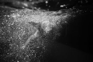 Black and white underwater photo of a swimmer surrounded by bubbles and light.