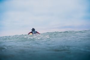 Surfer paddling through choppy ocean waves on overcast day.