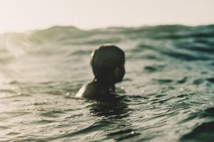 Person swimming in ocean waves during golden hour sunset light.