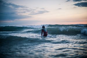 Person standing in ocean waves at sunset in wetsuit.