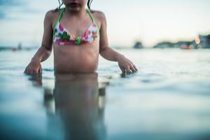 Young girl in floral bikini wading in shallow ocean water at dusk.