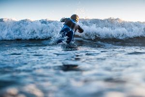 Surfer in wetsuit diving through a crashing wave in the ocean.