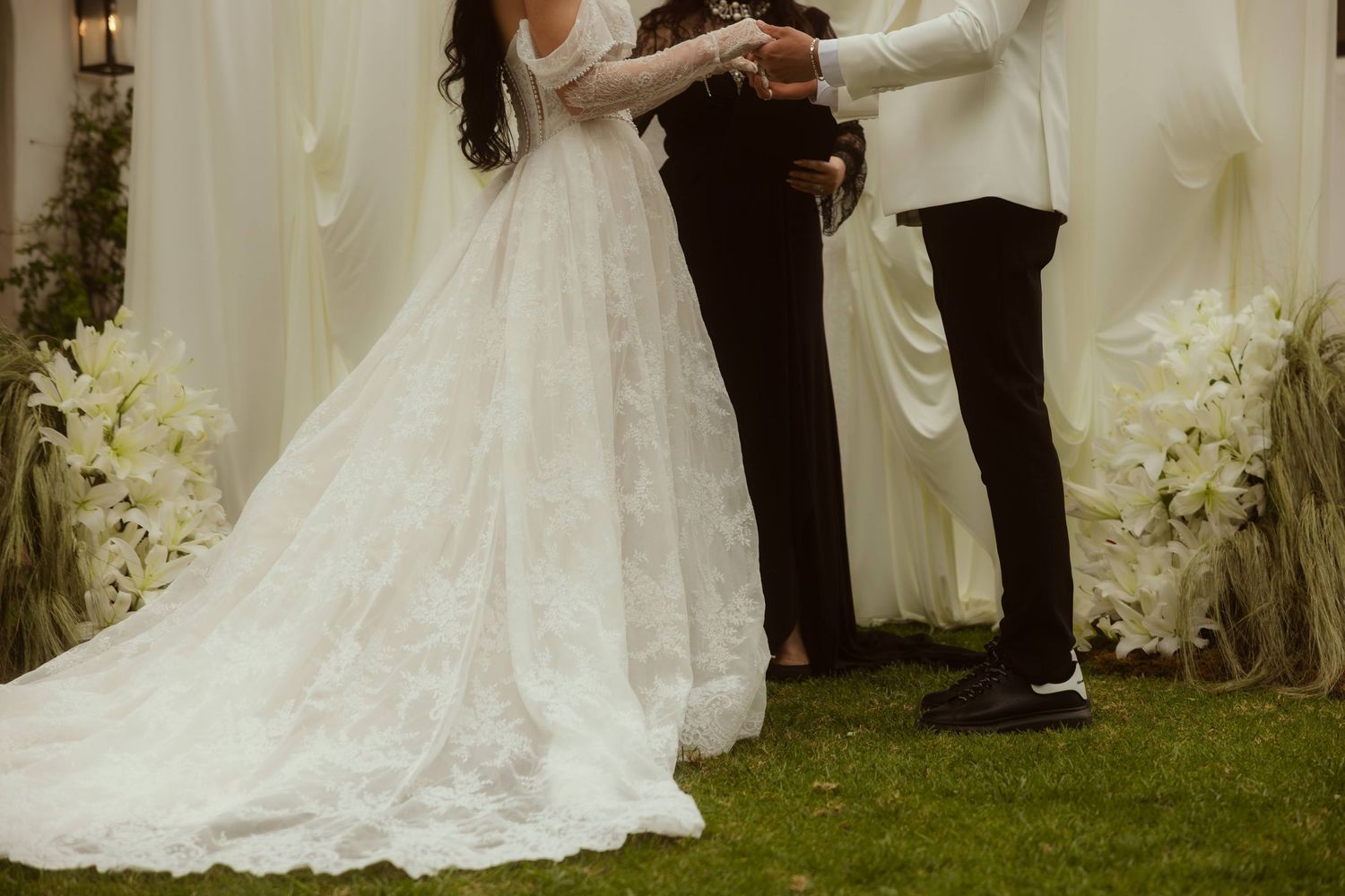 Bride in lace wedding gown and groom in white suit exchanging vows at an outdoor wedding ceremony during their Ojai elopement.