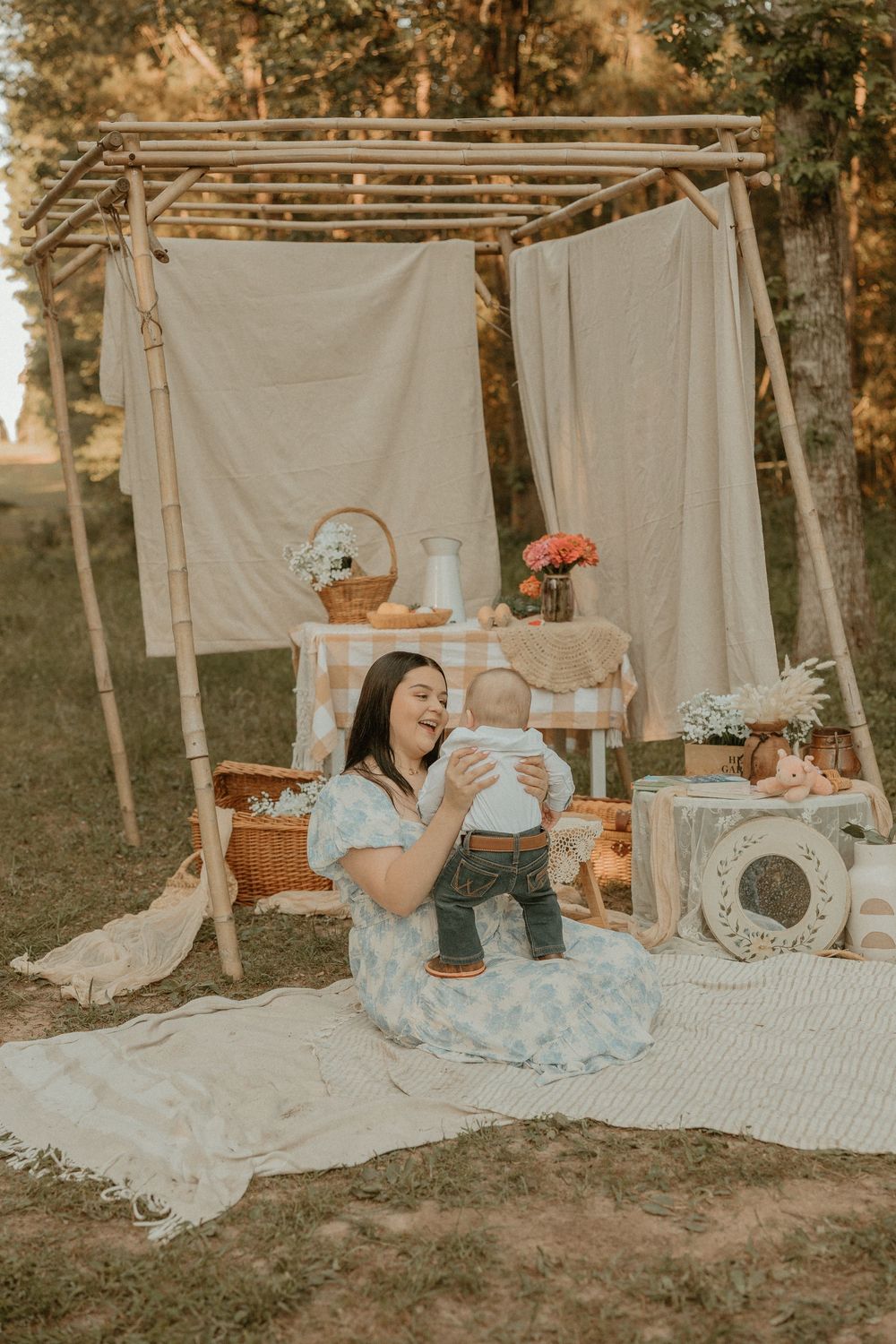 Rustic outdoor photo setup with vintage decor, white backdrop, and floral arrangements during golden hour lighting.