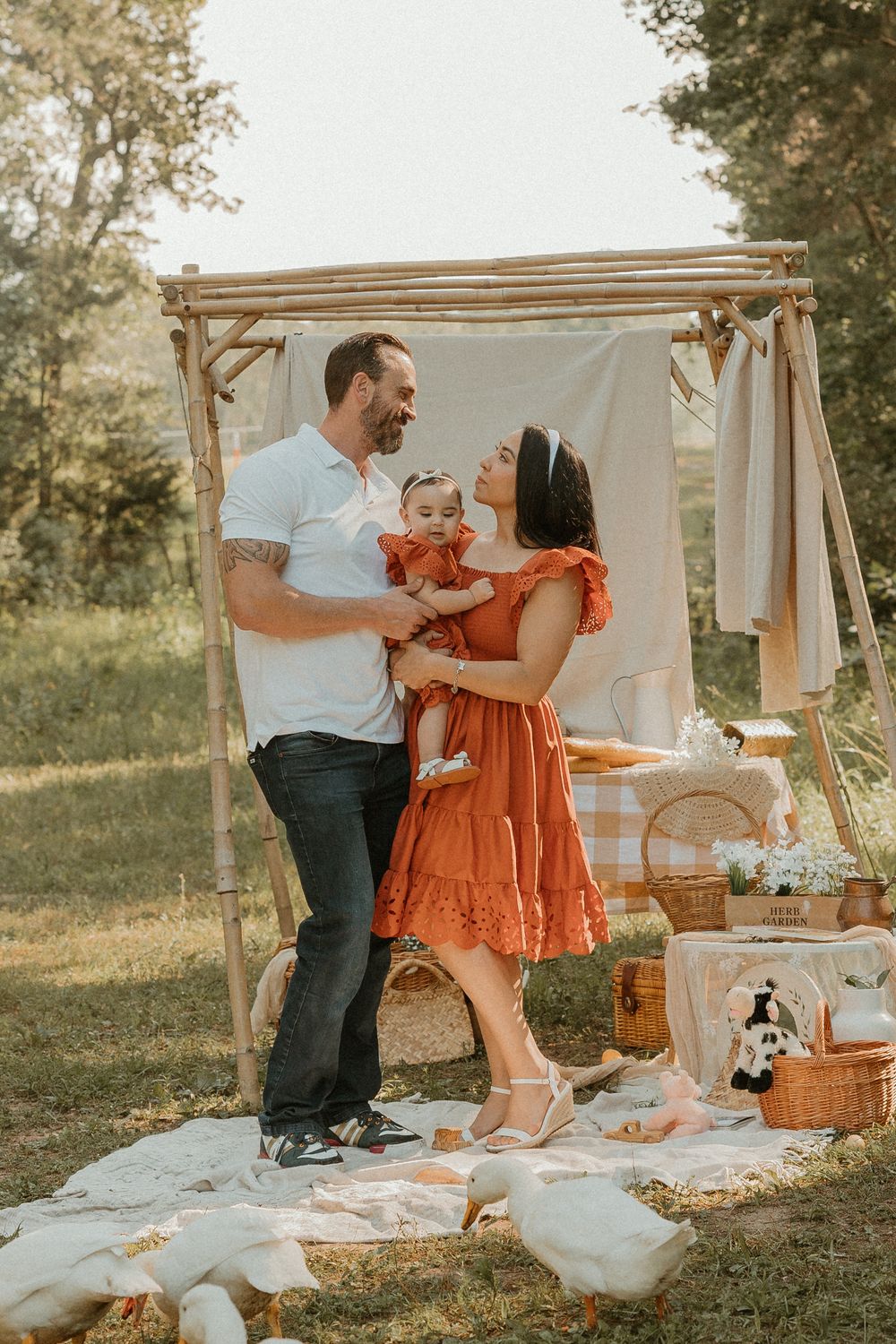 A family enjoys a picturesque outdoor picnic scene with wooden arbor and blankets on a sunny summer day.