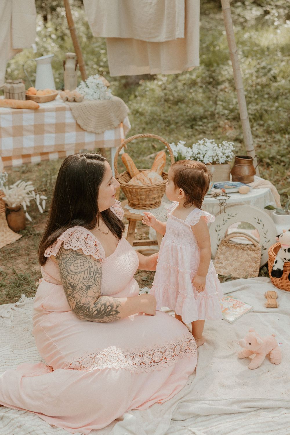 A mother and daughter in matching pink dresses enjoy a picturesque outdoor picnic with delicate floral decorations.