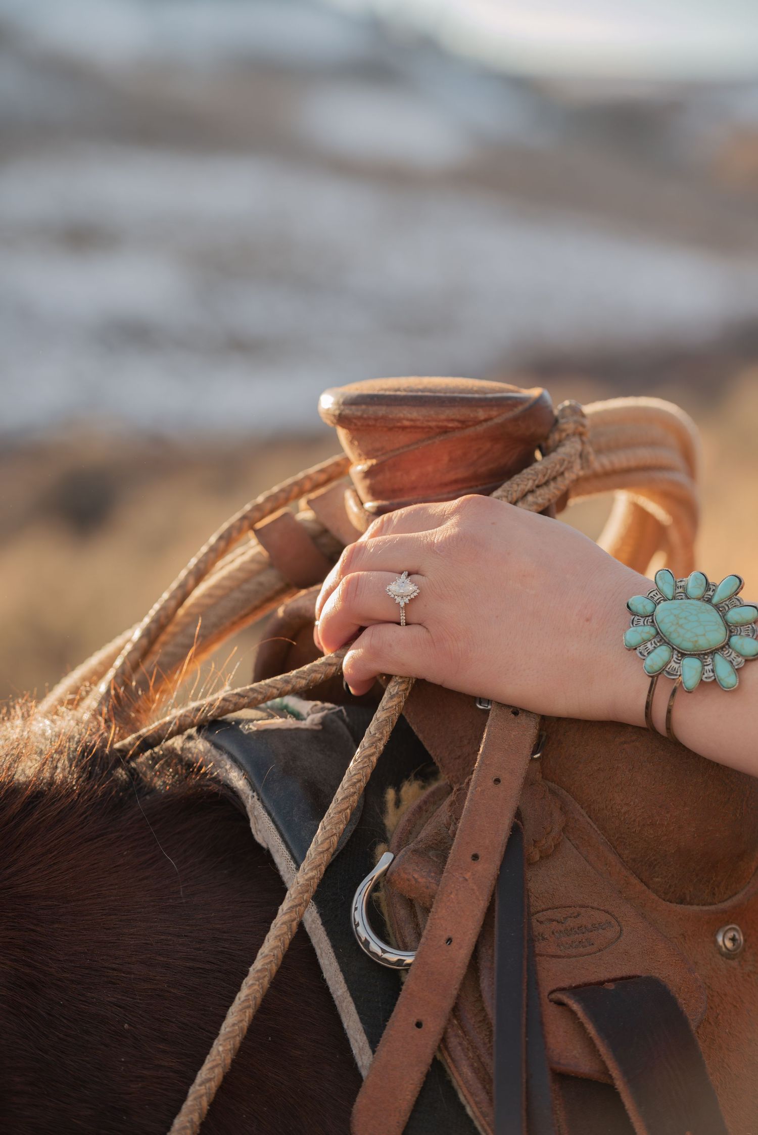 A western cowgirl wearing turquoise and a diamond ring in her cowboy engagement photos getting on her horse.