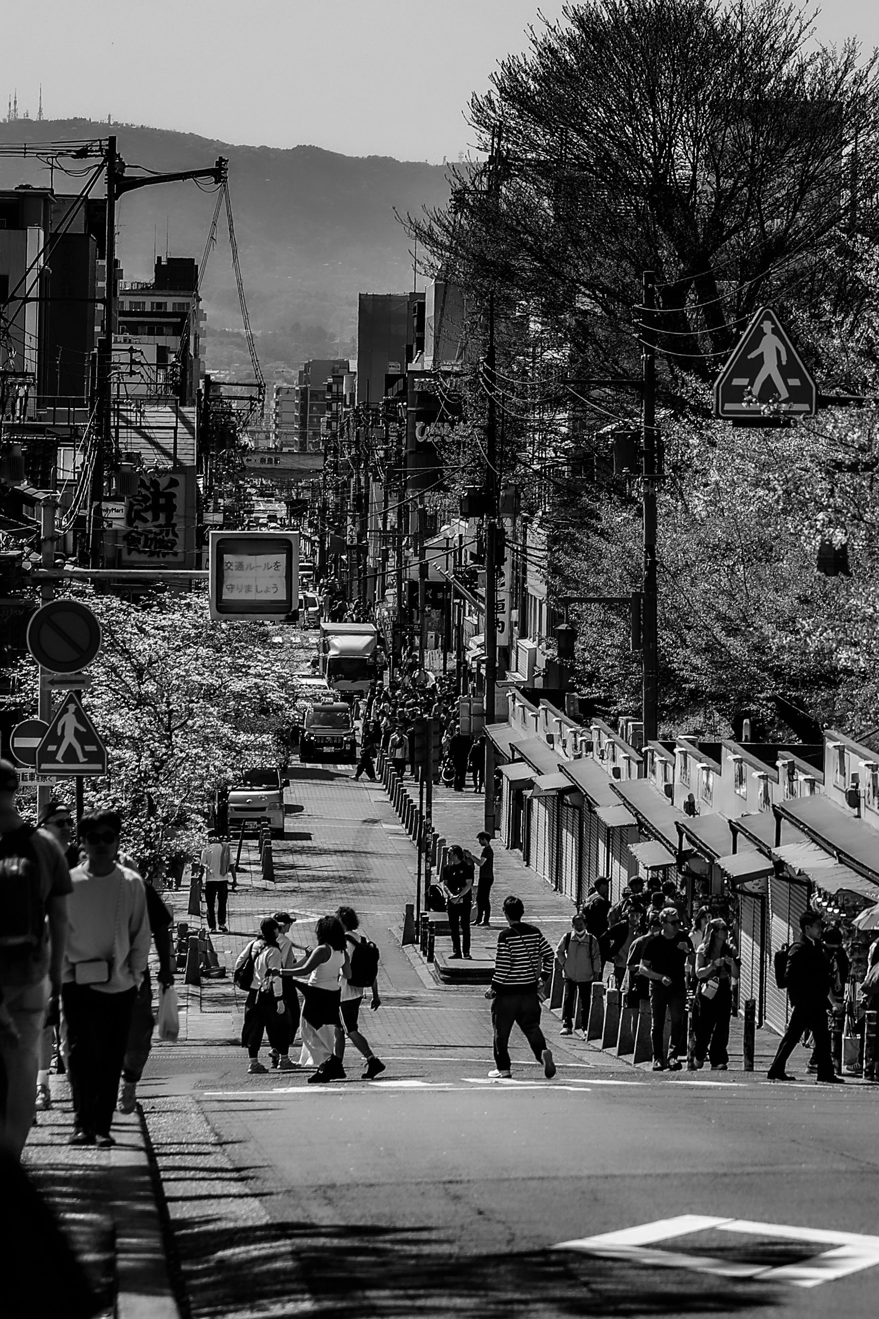 Black and white street scene in Nara, Japan with crowds of people walking along a busy urban road.