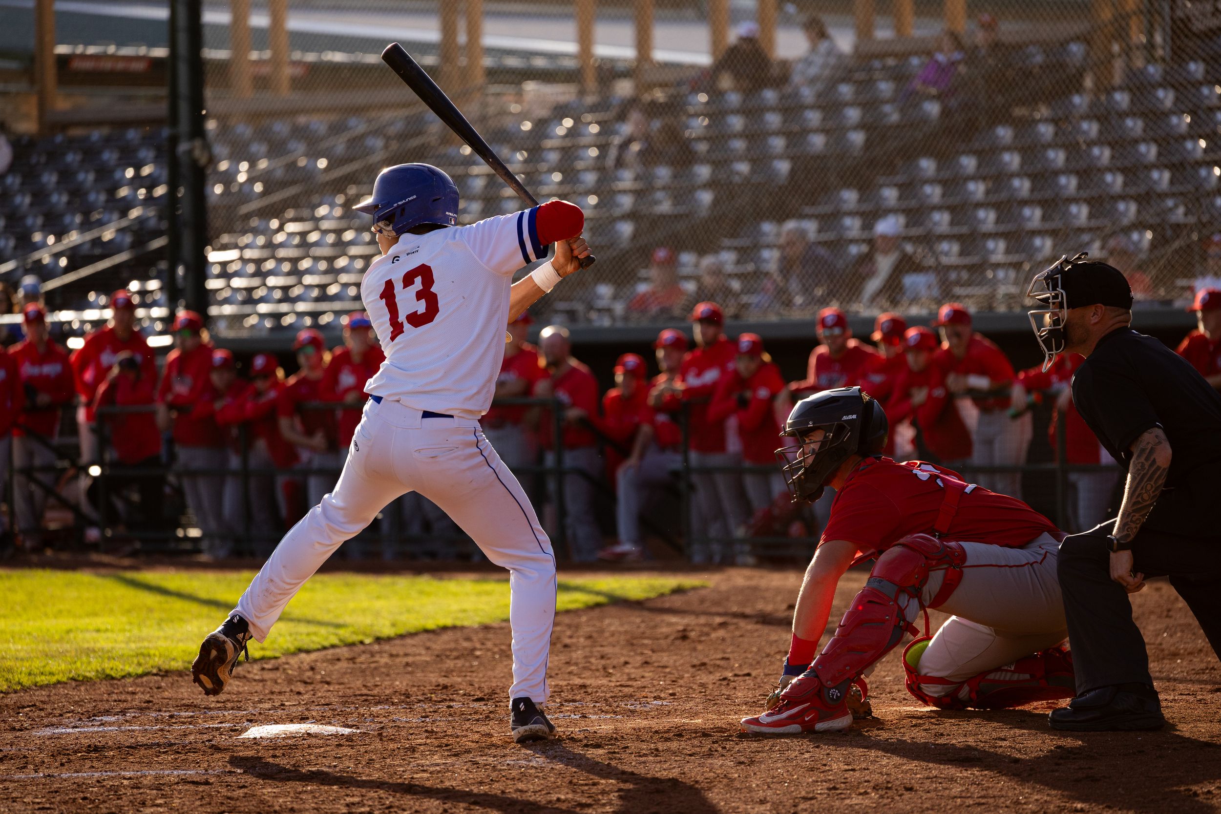 Brooks Bombers (WCBL) batter number 13 stands ready at plate with catcher and umpire at sunset.
