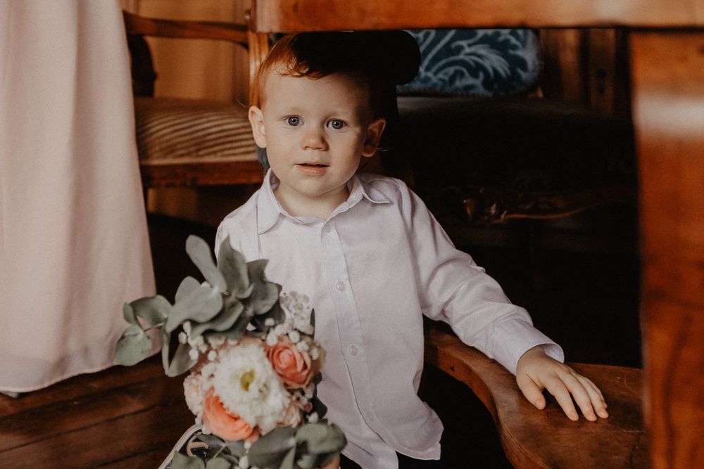 Adorable young boy in white shirt holding a pink floral bouquet at a wedding ceremony.