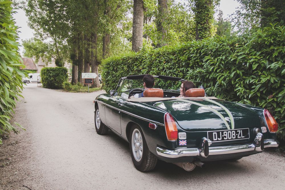 Classic green MG convertible sports car parked on a tree-lined driveway with tan leather interior.