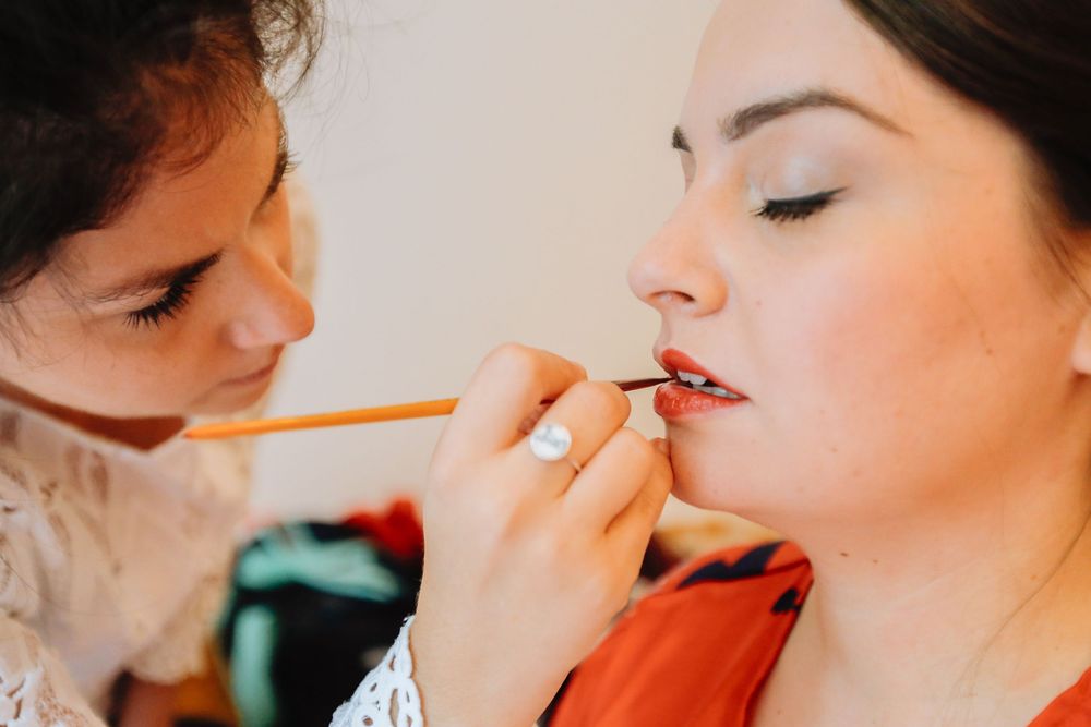 Makeup artist applying lipstick to bride with lip liner pencil before wedding.