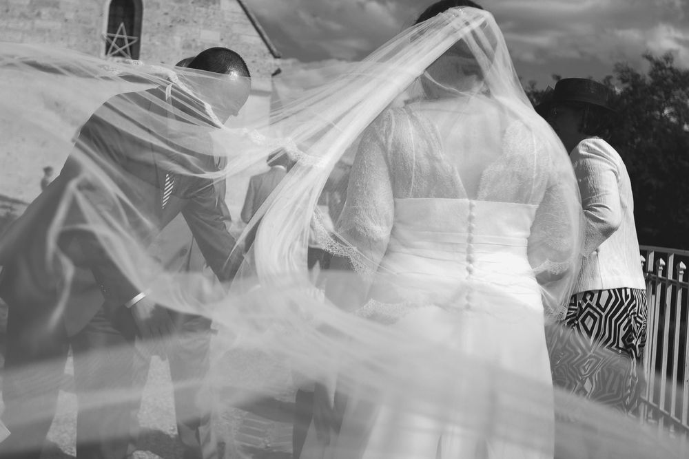 Black and white photo of bride and groom with flowing veil in the wind on their wedding day.