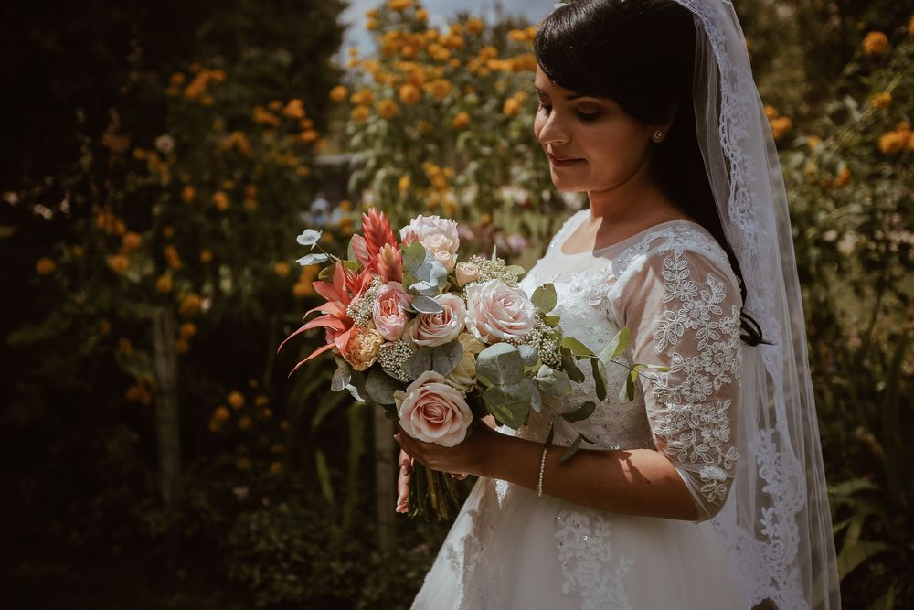 Bride in lace wedding gown holding pink and white bouquet in garden.