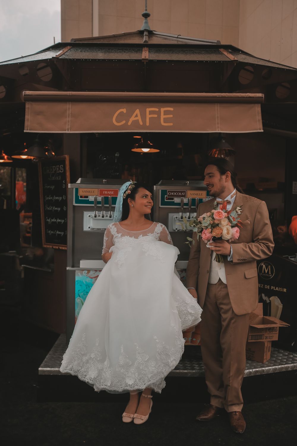 Bride and groom smiling together in front of a vintage cafe stand on their wedding day.