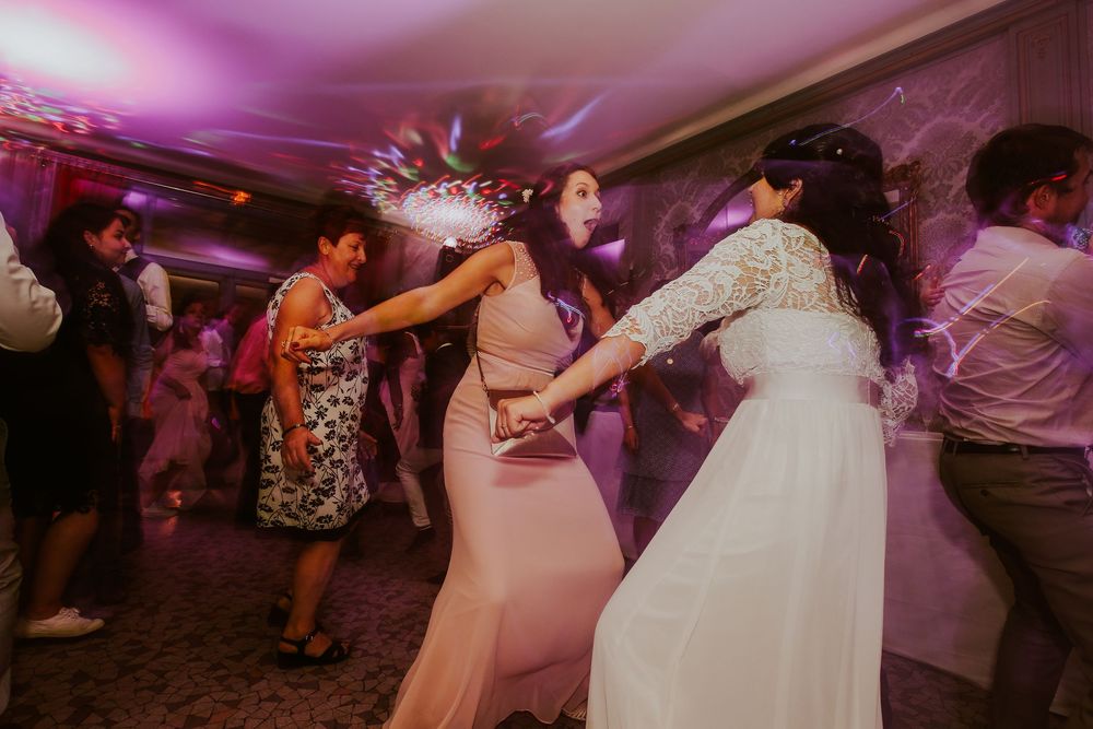 Bride and bridesmaids dancing joyfully at a wedding reception under colorful purple lights.