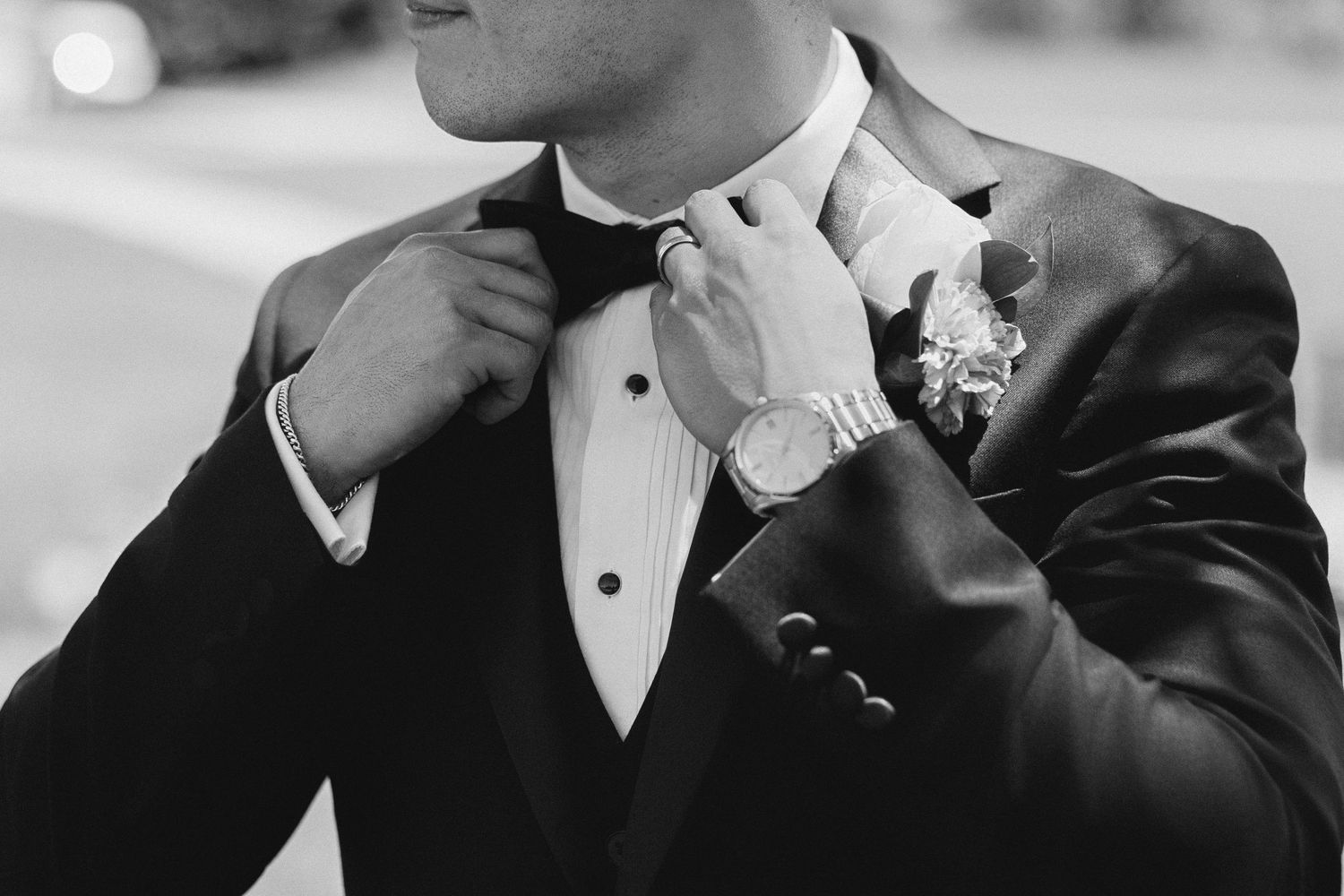 Groom in black tuxedo adjusting bow tie with boutonniere and watch, black and white wedding photo. williams farm pataskala, ohio