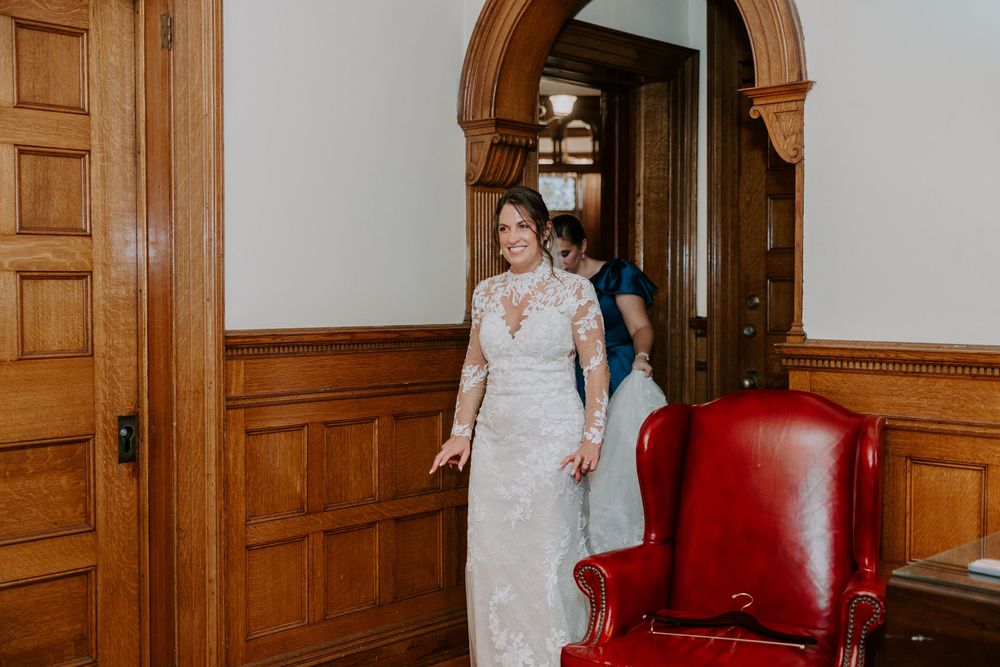 Bride in lace wedding dress smiling while walking through a wooden doorway.