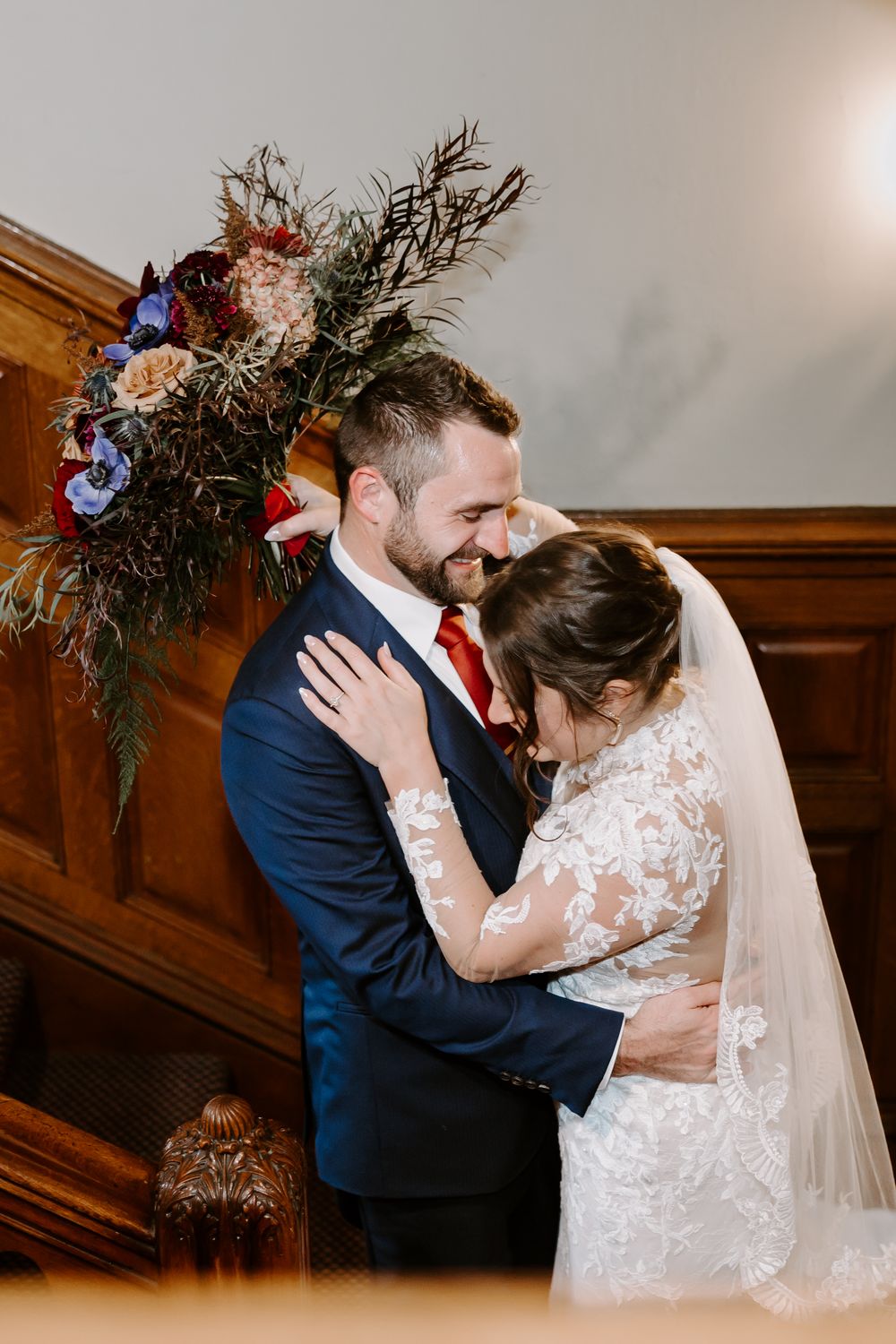 Bride and groom sharing a joyful embrace near a floral arrangement on a staircase.