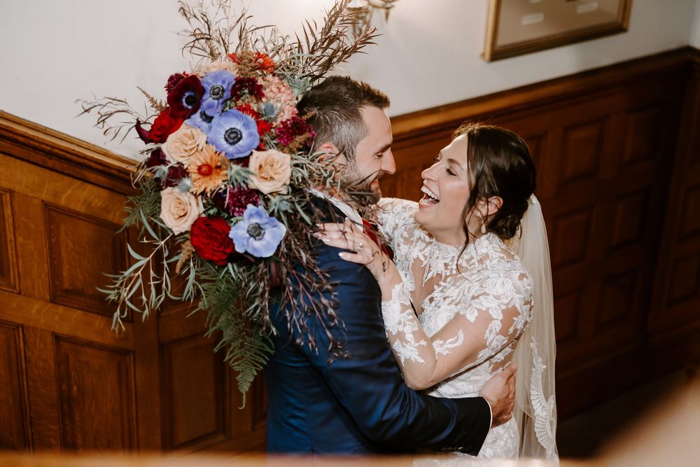 Bride laughing with groom while holding a bold bouquet of red, blue, and peach blooms.