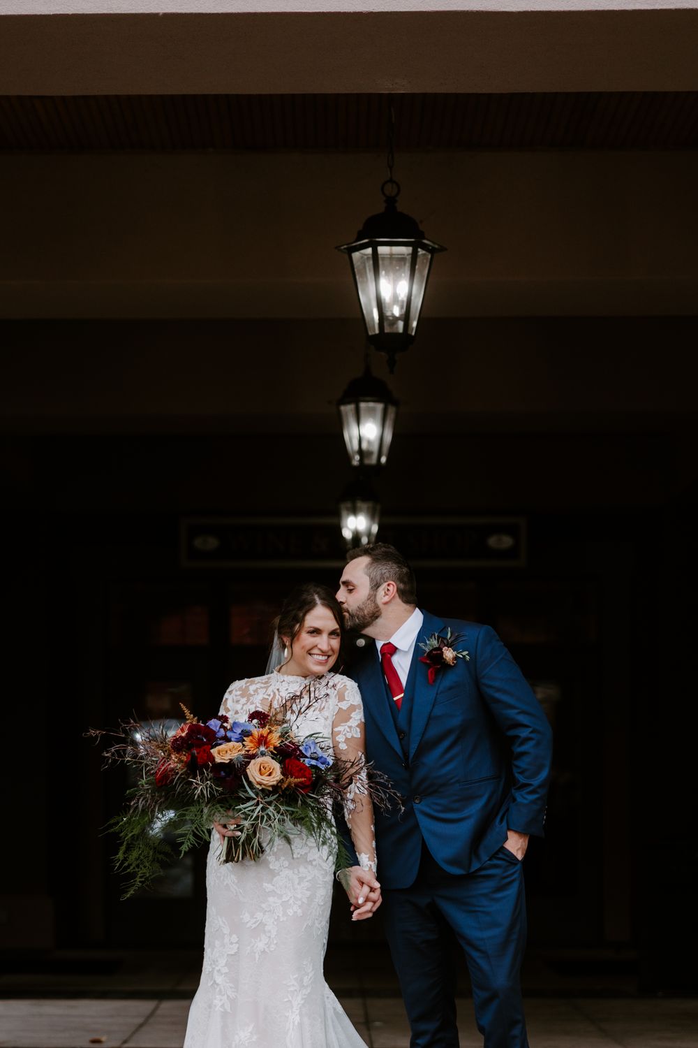 Bride and groom holding hands under vintage lanterns with a colorful bridal bouquet.