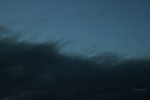 Dark storm clouds streak across a deep blue twilight sky in a moody abstract scene.