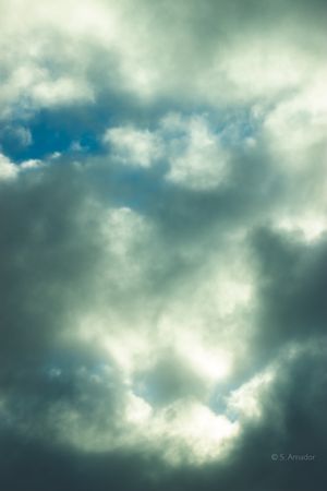 Dramatic cloudscape with billowing white and grey clouds parting to reveal patches of blue sky.