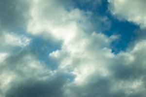Dramatic blue sky with billowing white and grey clouds forming a dynamic cloudscape on a partly cloudy day.