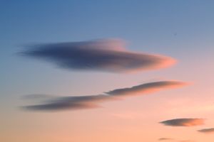 Dramatic lenticular clouds glowing pink and orange against a soft blue and peach sunset sky.