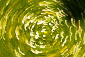 Abstract swirling motion blur of green grass and white flowers creating a vibrant circular vortex pattern.