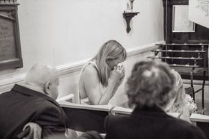 Black and white photo of wedding guest praying in church pew during ceremony.