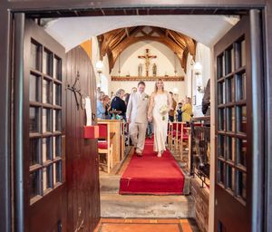 Bride and groom walking down the aisle viewed through open wooden church doors.