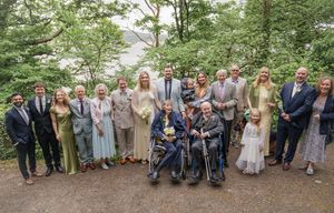 Large family group portrait at an outdoor wedding ceremony, posing together on a garden path surrounded by lush greenery.