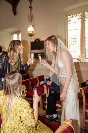 A bride in a white veil toasts champagne with guests inside a historic stone church.